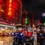 An image of two tuk-tuks in Bangkok’s Chinatown and neon lights in the background.