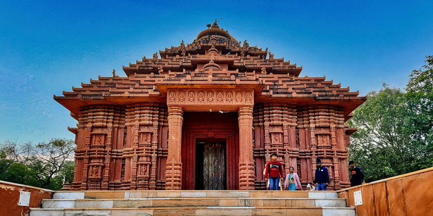 Ancient Hindu temple with a tall pyramidal roof and a central courtyard, featuring people standing at the entrance.
