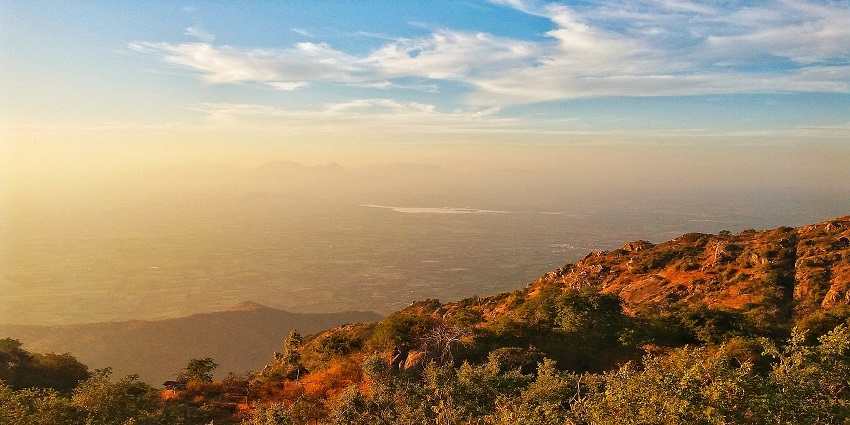 A breathtaking view of a sunset at Mount Abu, with the sun setting behind distant hills.