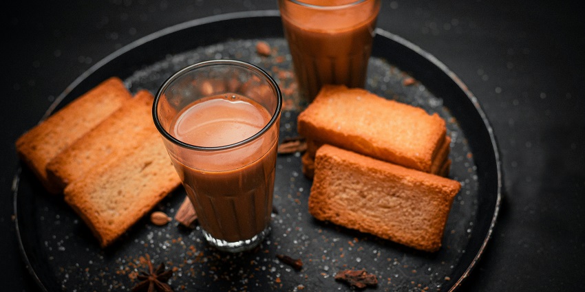 Plate of food with ruskit biscuits, chai cups, and various sides arranged neatly for a meal
