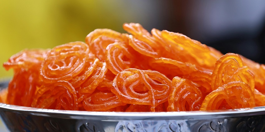 Delicious, juicy, and sweet Jalebi in bright orange colour served in a silver bowl.