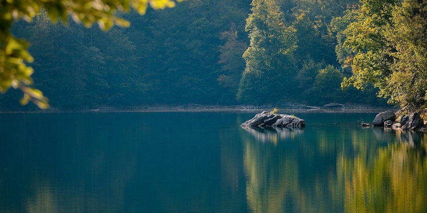 A peaceful view of a serene Surwal lake in Rajasthan surrounded by rocks and a lush forest.