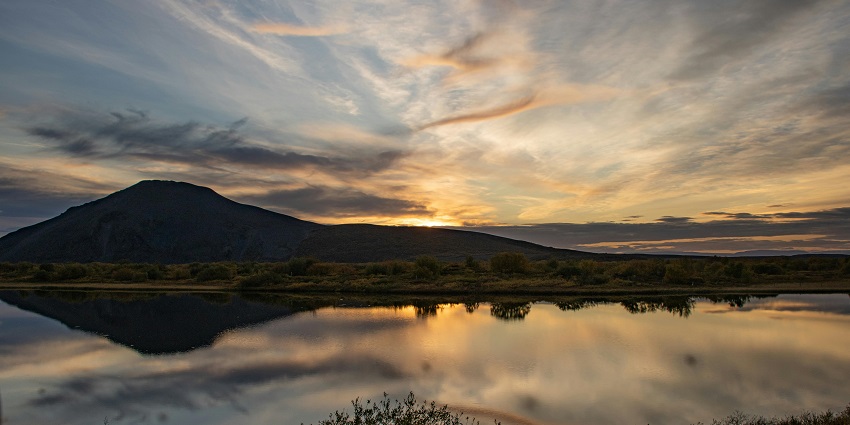 An image capturing the sunset view of a lake, with golden and blue sky over it in the day.