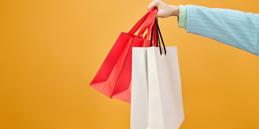 Hand holding colorful paper shopping bags against a muted background