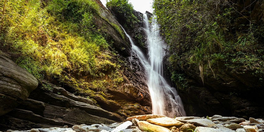 A picture of a waterfall slowly cascading down a hill surrounded by greenery and trees