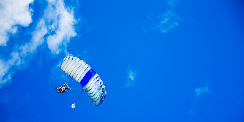 A couple paragliding in Pattaya, Thailand in a clear sky, in a black and white parachute.