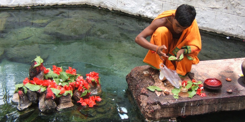 A priest performing puja at the Taptapani Hot Springs with devotees in the background