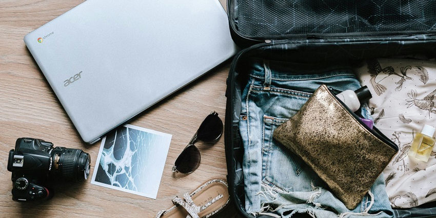 A black DSLR camera rests beside sunglasses and a bag captured on a flat surface.