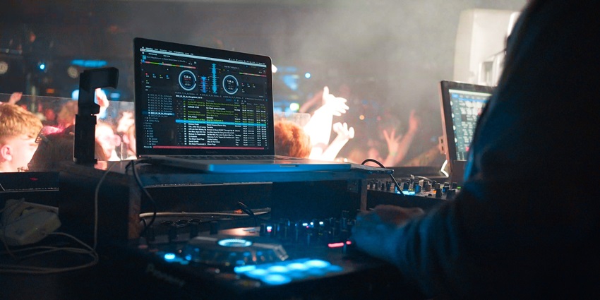 DJ performing at a party, using a mixing console, surrounded by colourful lights.