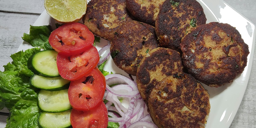A glimpse of round and soft kebabs served with chopped onion, tomato, and cucumber.