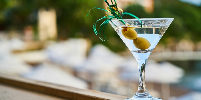 Close-up of a martini glass with green olives on a skewer, set against a blurred background