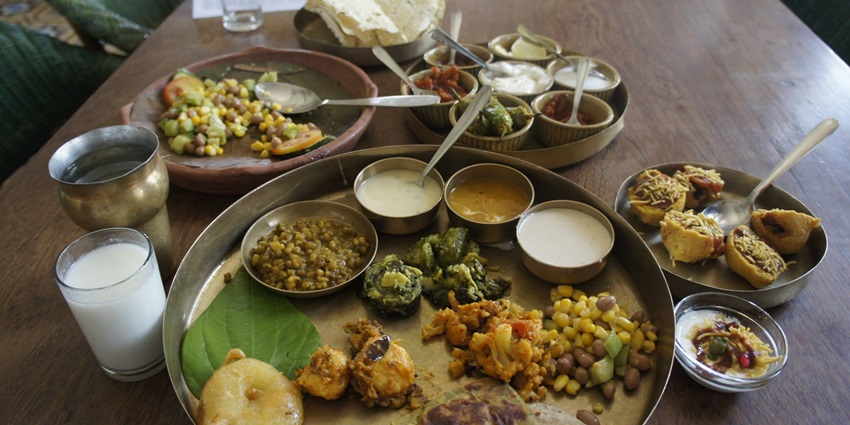 Colourful Gujarati thali featuring multiple vegetarian dishes, curries, and flatbreads.