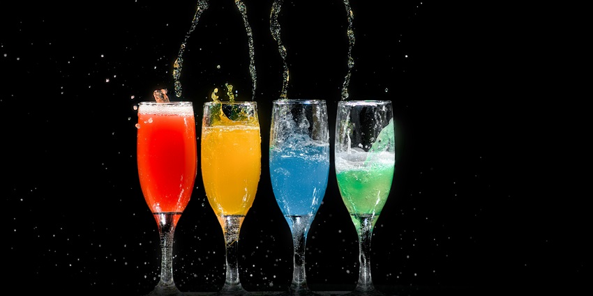 A tempting view of four glasses with colourful drinks splashing out sitting on a table.