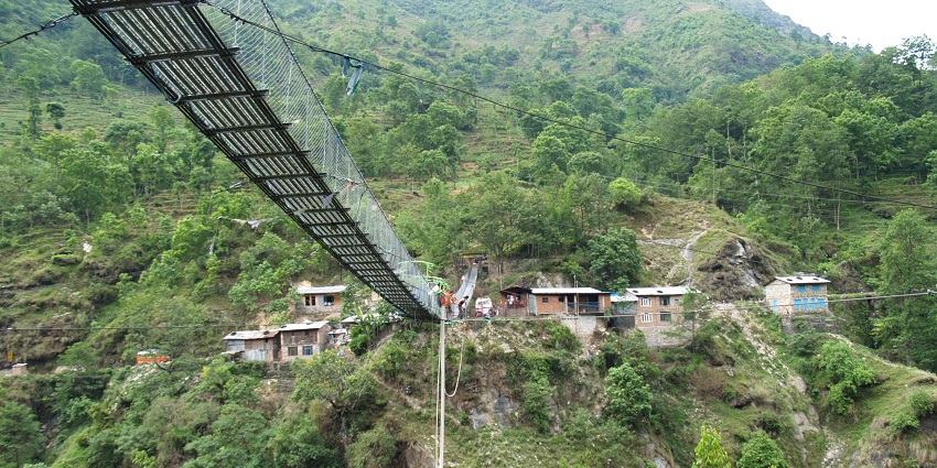 A suspension bridge at The Last Resort with lush green hills and a river below.