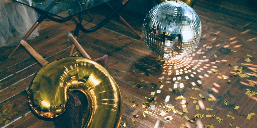A mesmerising view of a silver disco ball with inflated golden balloons on the side.