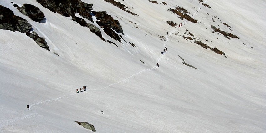 Trekkers navigating a snow-covered slope at Sar Pass, with majestic mountain peaks in view