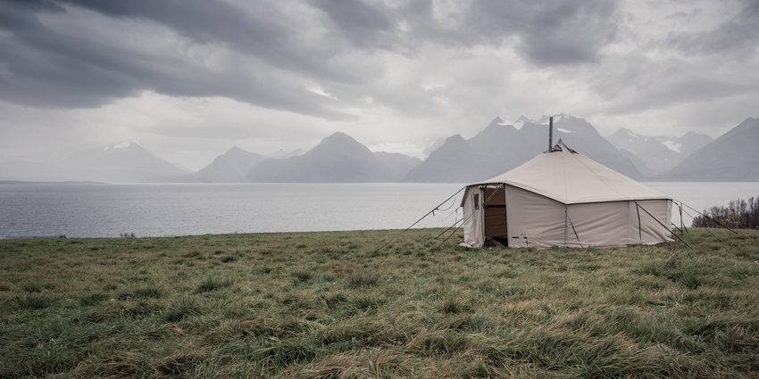 A tent set up on a sandy beach overlooking the sea, with clouds and a vast ocean in the background.