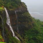 A beautiful waterfall cascading down rocky terrain surrounded by greenery in Matheran.