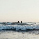 Two people standing in the middle of a beach enjoying water waves.