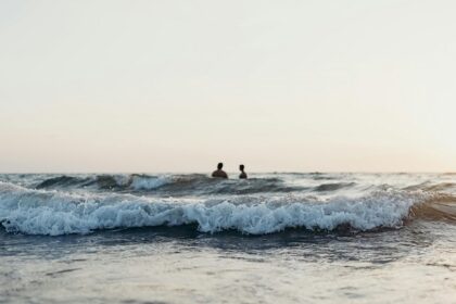 Two people standing in the middle of a beach enjoying water waves.