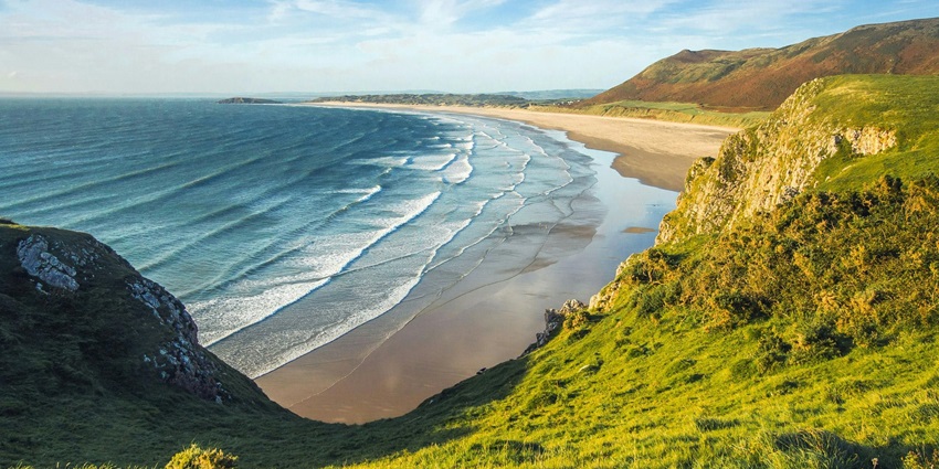 Rocky beach with clear blue sea and sandy shore, reflecting coastal beauty during the day.