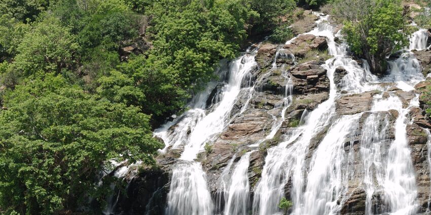 The water cascades through the cliffs surrounded by greenery.