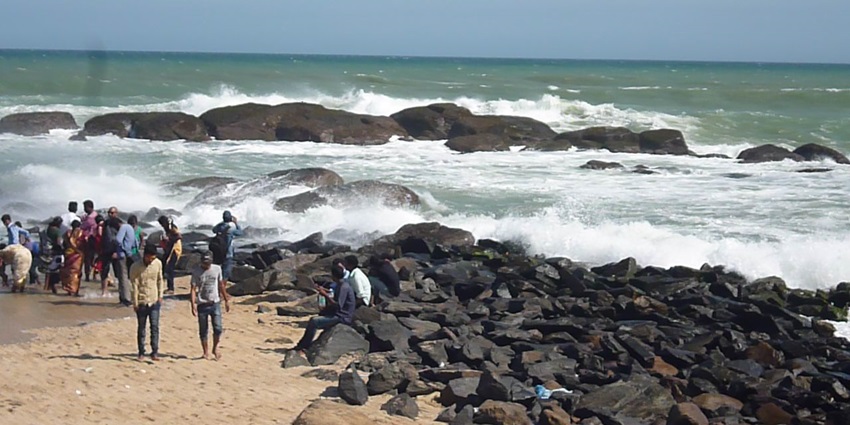 A picture of people relaxing at a confluence of rivers with rocks all around the river bank