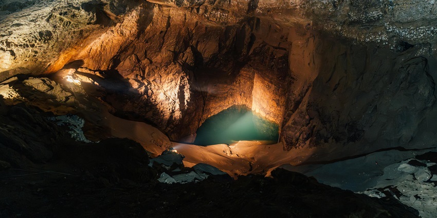 A man with a headlamp and a utility bag observing the formations in the Kutumsar Caves.