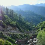 A scenic view of Tosh village in Himachal Pradesh with distant mountains.