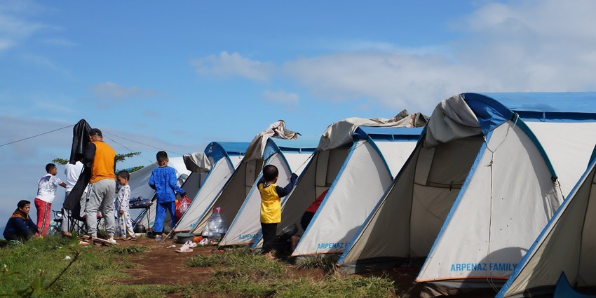 A family camping in Tosh with multiple tents and a picnic on a grassy field surrounded by trees.