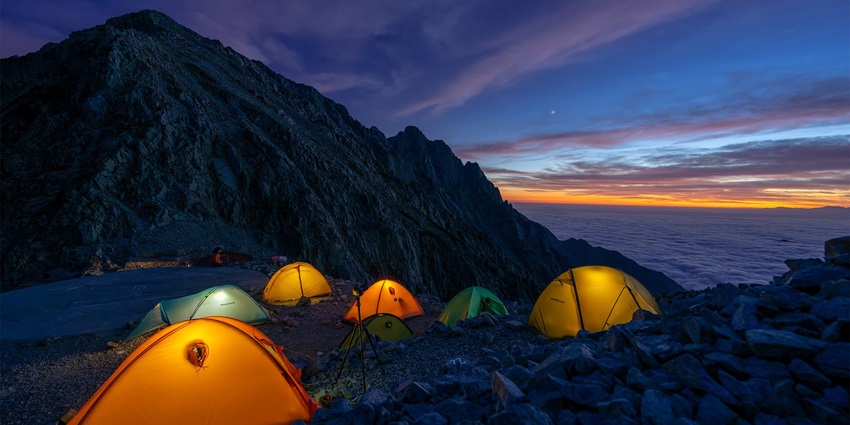 A serene mountain landscape with a glowing tent at sunset, surrounded by lush greenery, similar to camping in Tosh.