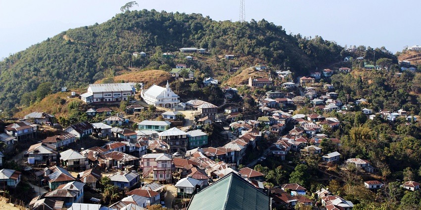 Picturesque view of a hilly town in Mizoram, surrounded by lush greenery under clear blue sky.