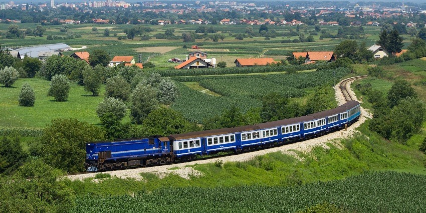 Train travelling through lush green landscapes with mountains and clear blue sky