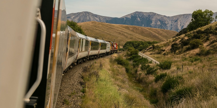 A white train travels through a scenic landscape with mountains in the distance.