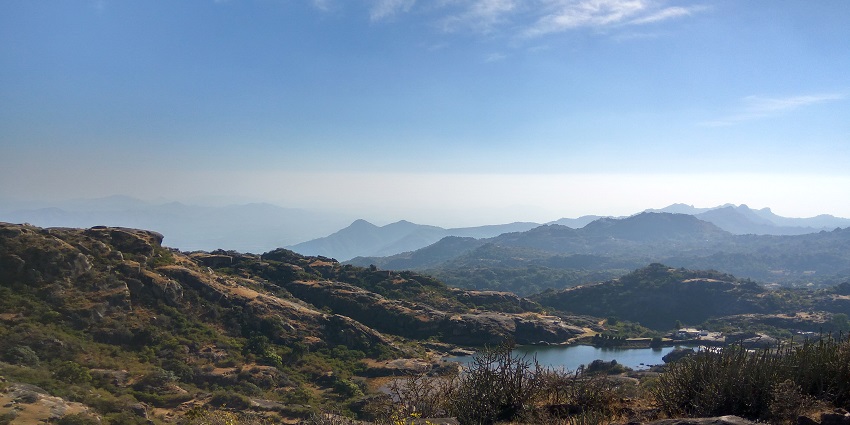 Scenic view of Mount Abu, showcasing rolling hills, lush greenery, and rocky outcrops under a clear blue sky