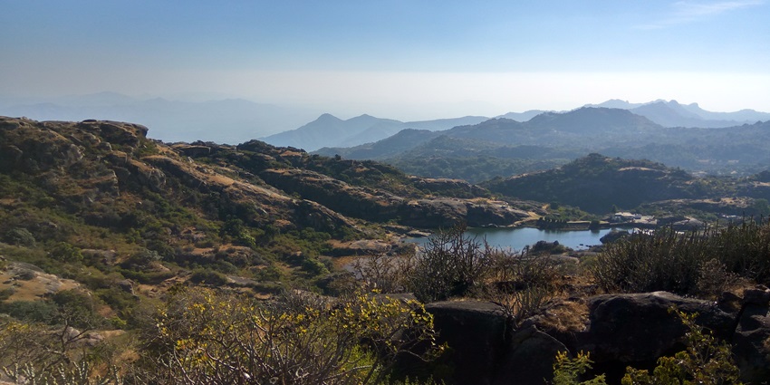 Scenic view of Mount Abu, showcasing rolling hills, lush greenery, and rocky outcrops under a clear blue sky.