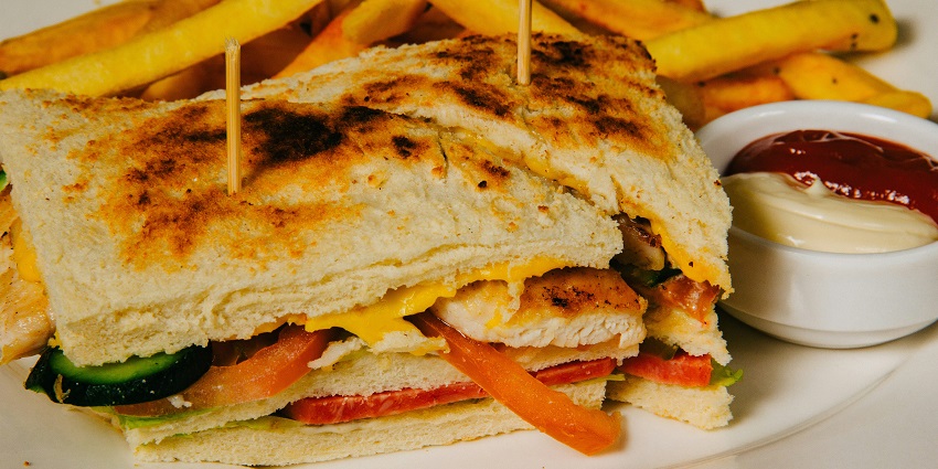 A mouth-watering view of a sandwich filled with assorted vegetables with a classic dip.