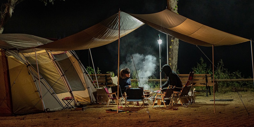 A group of friends enjoying Camping in Tosh with tents, sitting around a cosy fire in the forest.