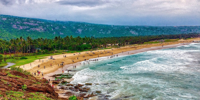 Panoramic image of a scenic beach surrounded by ocean and lush trees
