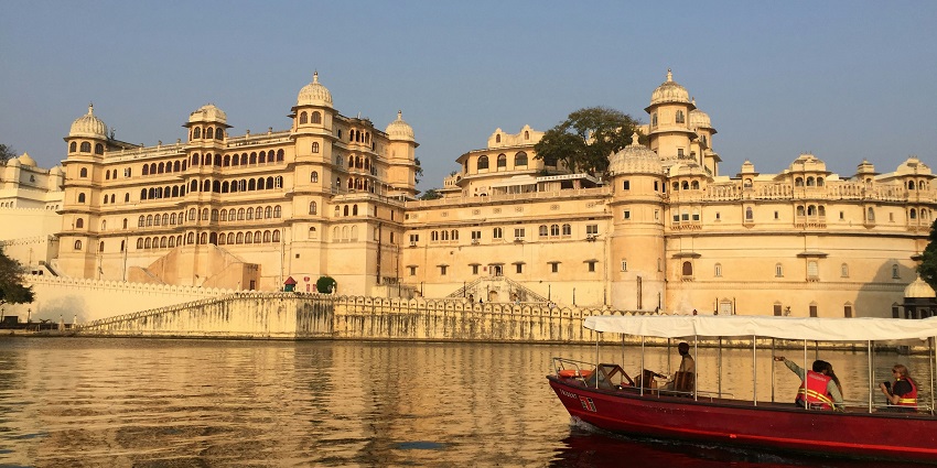 A view of the City Palace of Udaipur reflecting in Lake Pichola during golden hour twilight.