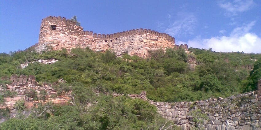 A picture of a fort wall on top of a hill taken from the hill base with greenery all around
