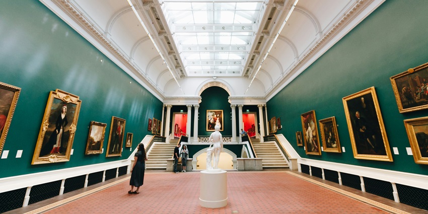 Visitors seated on chairs inside a modern art gallery surrounded by contemporary artworks