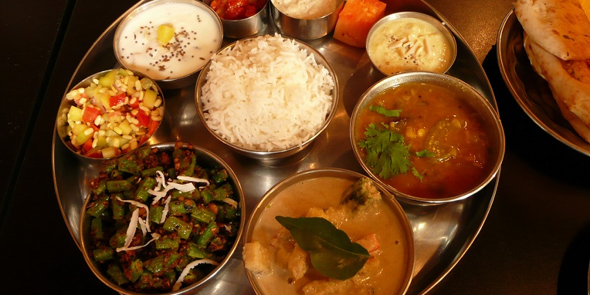 Indian thali with various dishes served on a metal plate, including rice, curry, and vegetables, offering a diverse culinary experience.