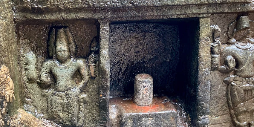 A picture of a historical temple with stone sculptures of deities amidst lush greenery