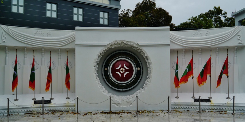 Victory Monument in Malé with a red, green, and white emblem at its base, set against a palm trees