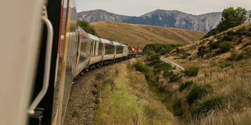 Image of railways tracks and trains surrounded by the mountains, under clear blue sky.