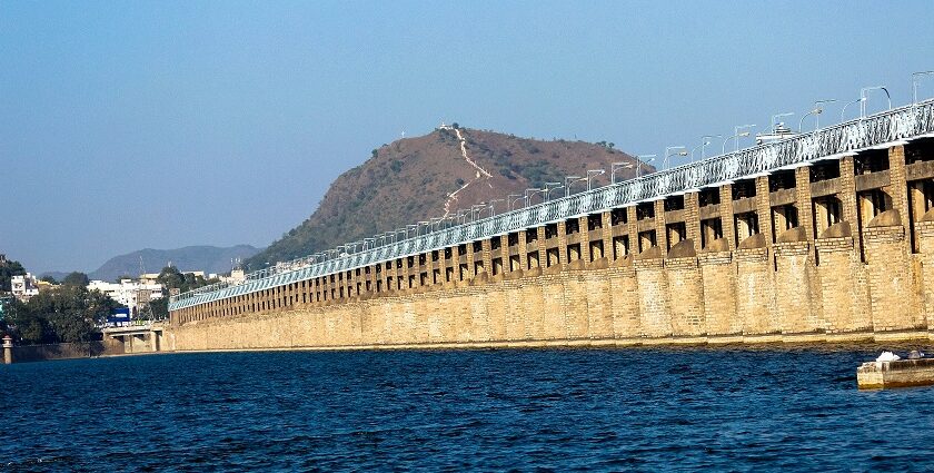 A picture of a bridge crossing a river with boats sailing in the river and a hill in the background