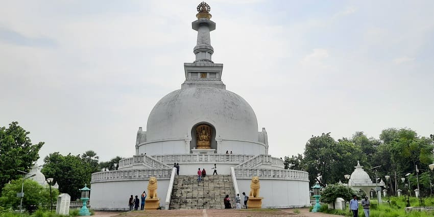 A picture of a tall stupa with white exteriors having visitors praying and admiring