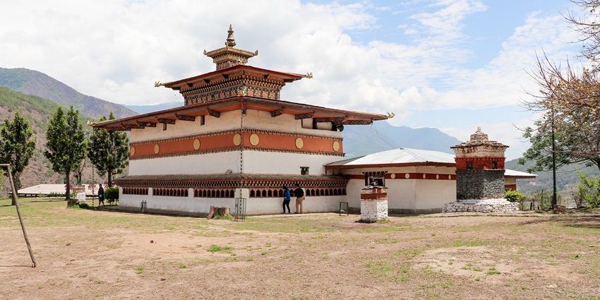 Chimi Lhakhang temple perched on hillock, monks and visitors strolling in green courtyard