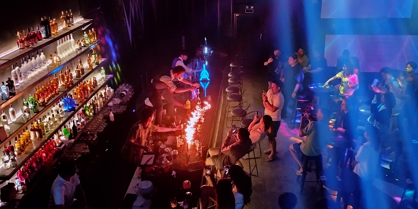Bartenders displaying a fire show using spirit; people enjoying and clicking pictures.